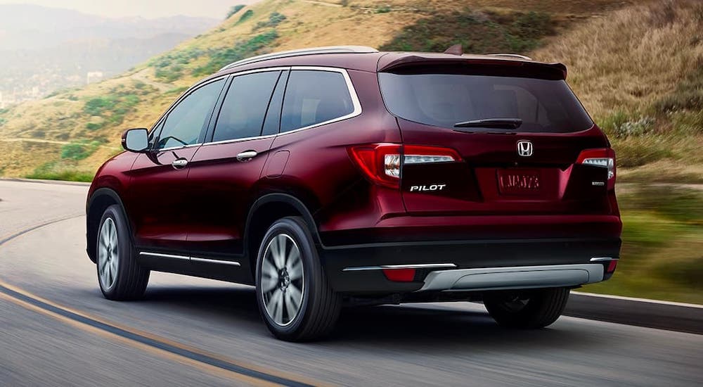 A burgundy 2021 Honda Pilot is shown from a rear angle while driving on a highway.