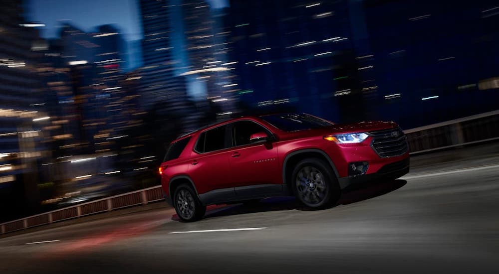 A red 2021 Chevy Traverse is driving in a city at night after winning the 2021 Chevy Traverse vs 2021 Honda Pilot comparison.