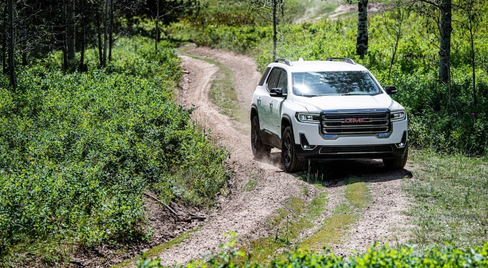A white 2021 GMC Acadia AT4 is driving on a trail in the woods.