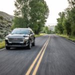 A black 2021 GMC Acadia Denali is driving on a highway.