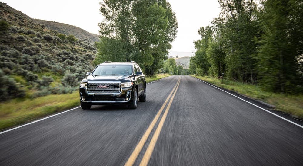 A black 2021 GMC Acadia Denali is driving on a highway.