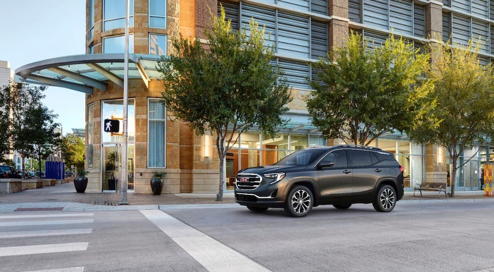 A dark gray 2021 GMC Terrain is parked at a stop sign on a city street.
