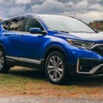 A blue 2021 Honda CR-V is parked in front of a photographer and a lake.