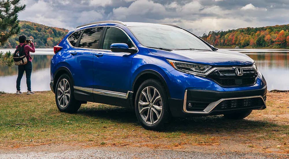 A blue 2021 Honda CR-V is parked in front of a photographer and a lake.