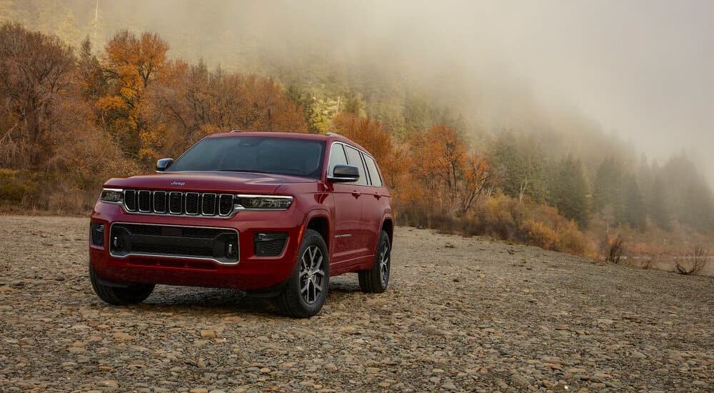A red 2021 Jeep Grand Cherokee L is parked on rocks in front of a misty mountain.