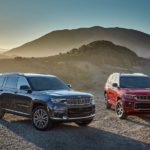 A black and a red 2021 Jeep Grand Cherokee L are parked on a hill in front of misty mountains.