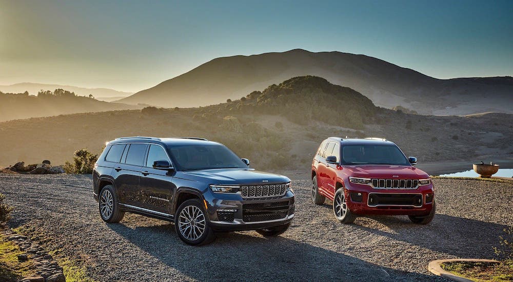 A black and a red 2021 Jeep Grand Cherokee L are parked on a hill in front of misty mountains.