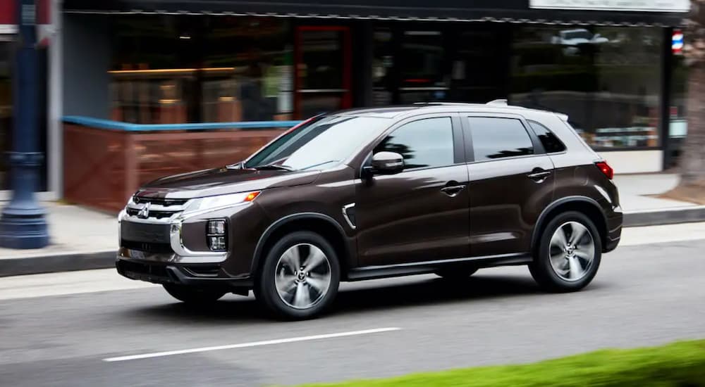 A dark brown 2021 Mitsubishi Outlander Sport is driving on a city street.