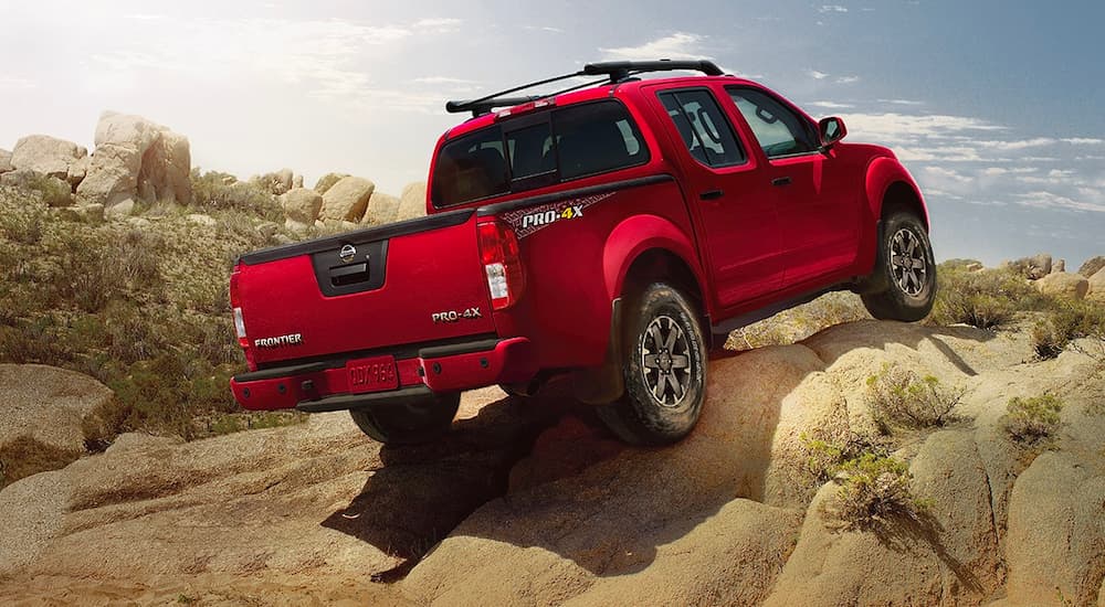 A red 2021 Nissan Frontier Pro4x is shown from the rear driving over a rock pile.