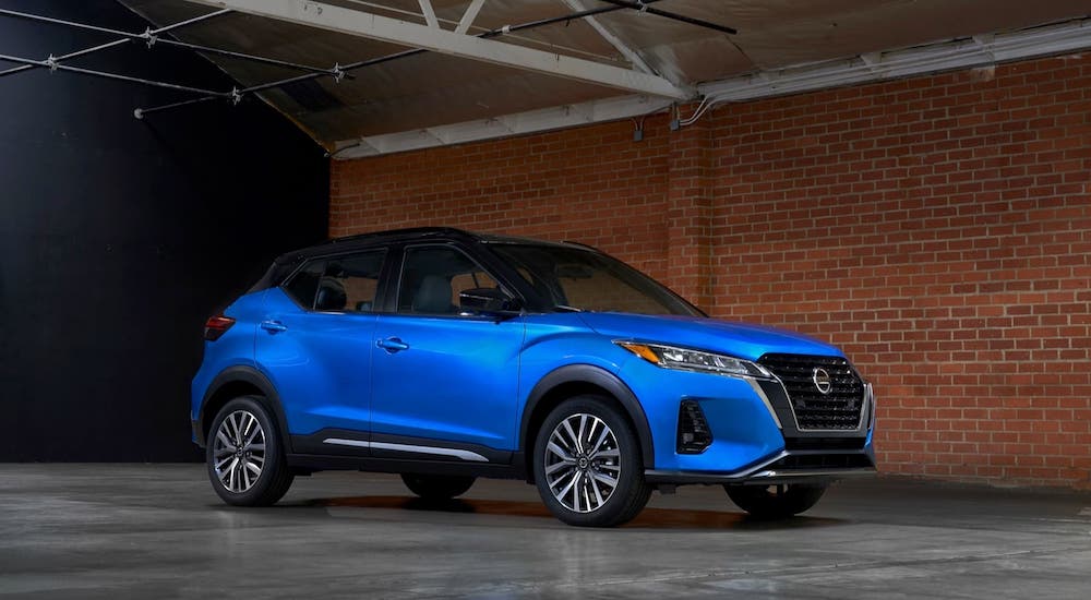 A blue 2021 Nissan Kicks is shown from the side parked in front of a red brick wall.