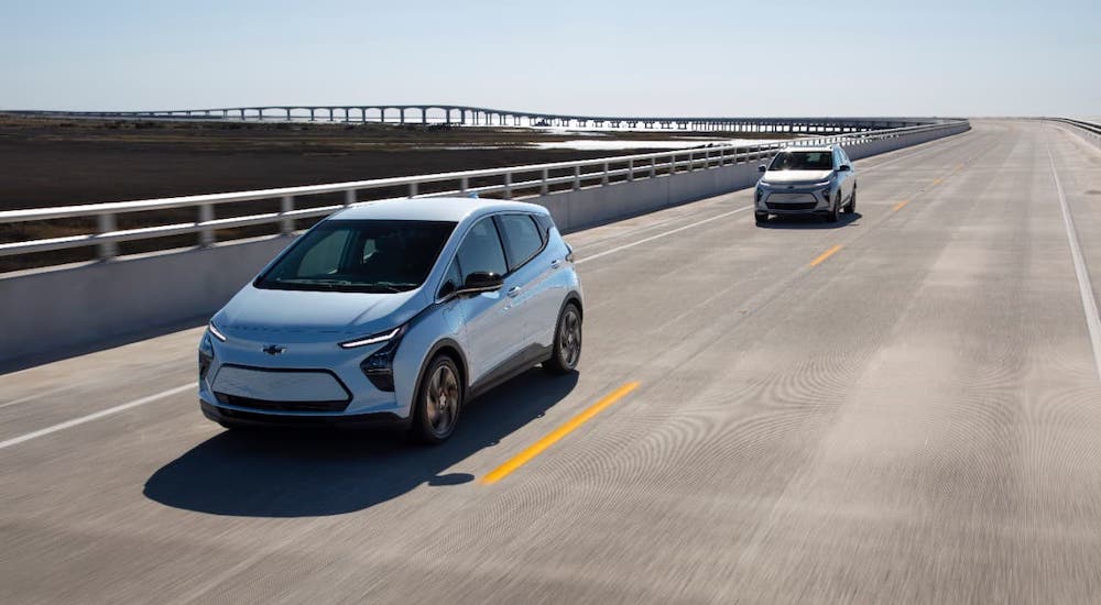 A pale blue 2022 Chevy Bolt EV is driving on a highway in front of another car.