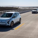 Two silver 2022 Chevy Bolt EVs are driving on an empty highway.