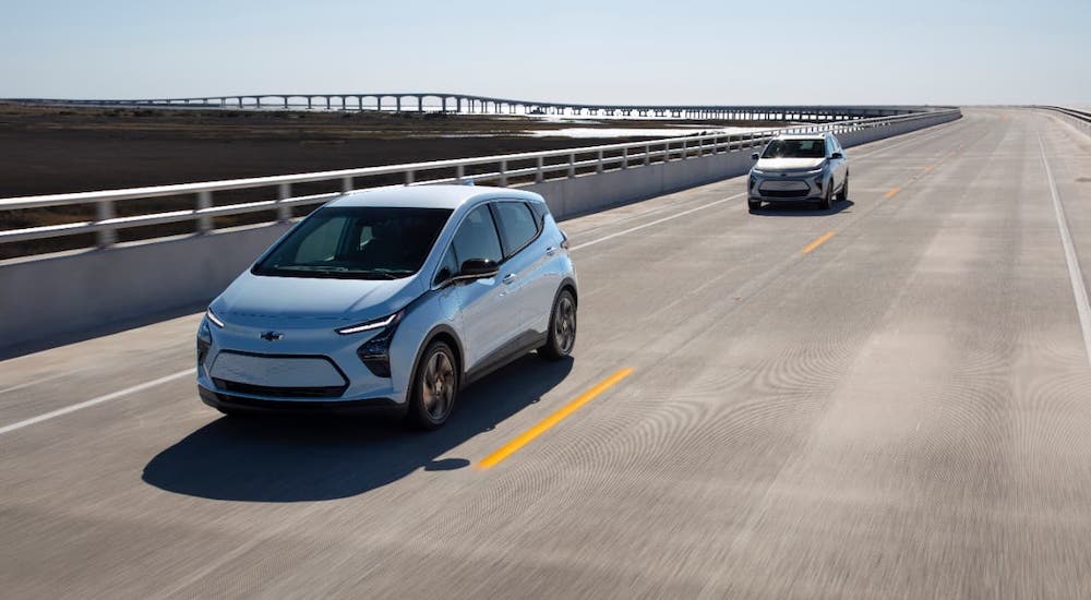 Two silver 2022 Chevy Bolt EVs are driving on an empty highway.