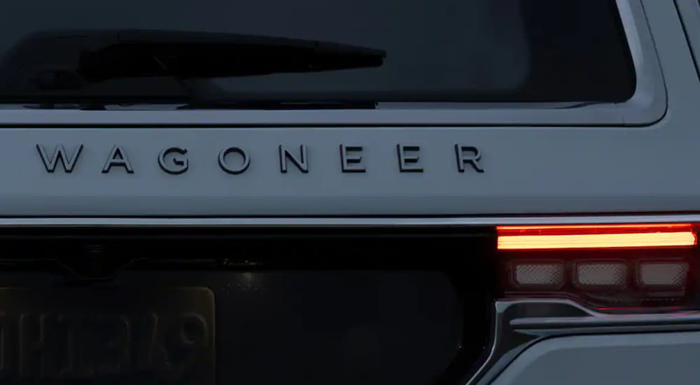 The rear logo of a white 2022 Grand Wagoneer is shown at dusk.