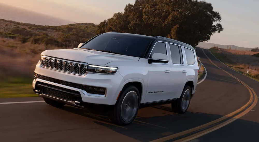 A white 2022 Grand Wagoneer is shown from an angle driving on an open road.