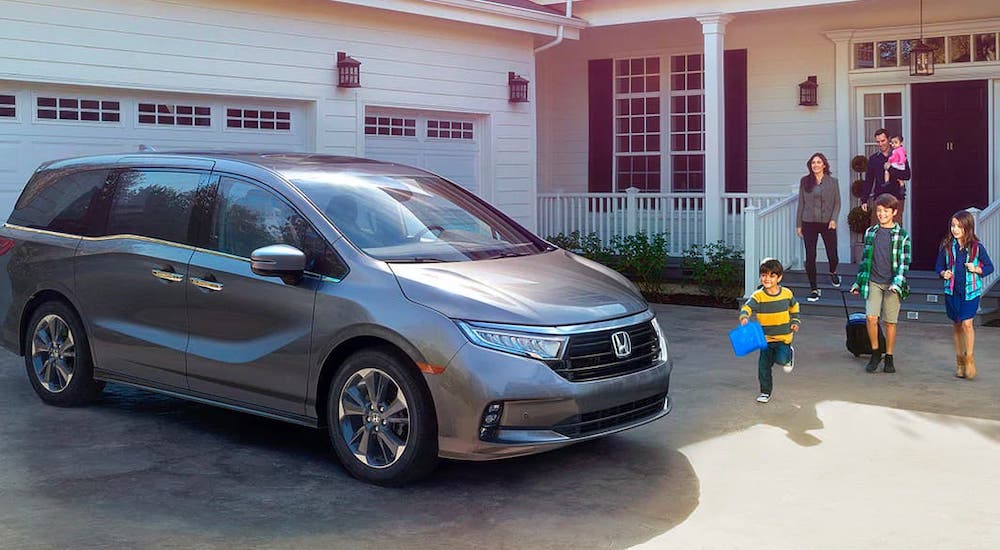 A family is walking towards a gray 2022 Honda Odyssey that is parked in front of a home.