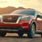 A red 2022 Nissan Pathfinder is on dirt in front of mountains at sunset.