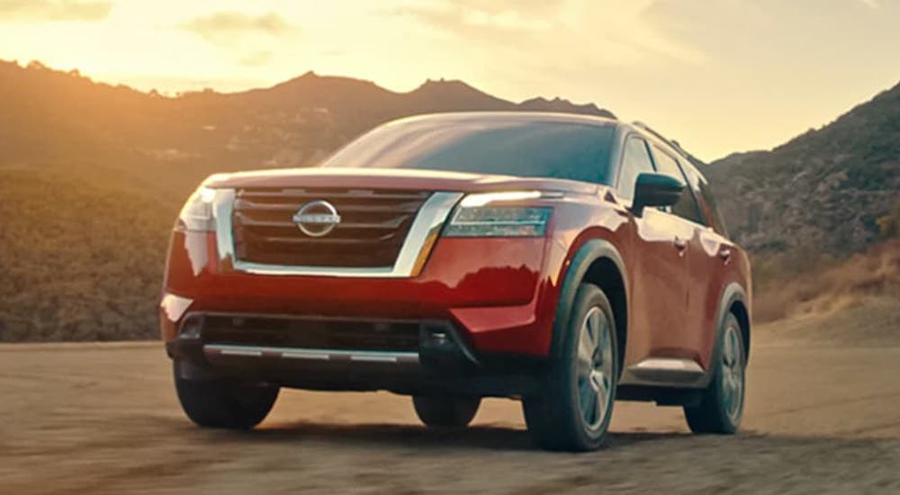 A red 2022 Nissan Pathfinder is on dirt in front of mountains at sunset.