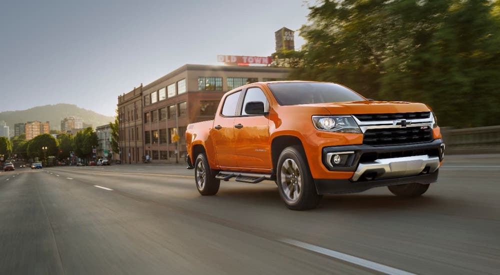 An orange 2021 Chevy Colorado is driving on a city street.