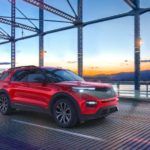 A red 2021 Ford Explorer ST is shown driving over a bridge at sunset.