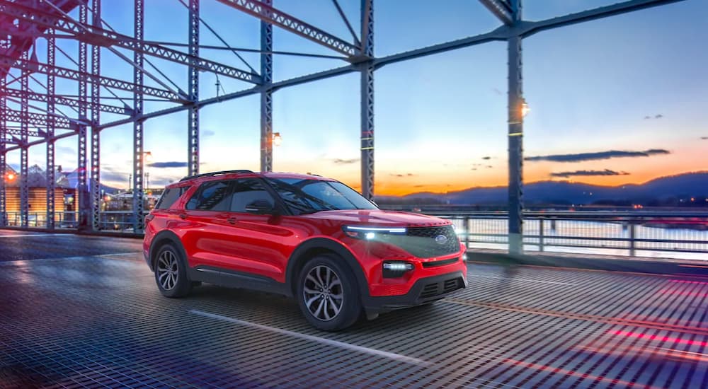 A red 2021 Ford Explorer ST is shown driving over a bridge at sunset.