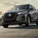 A gray 2021 Nissan Kicks is driving away from the city after leaving a Nissan Dealership
