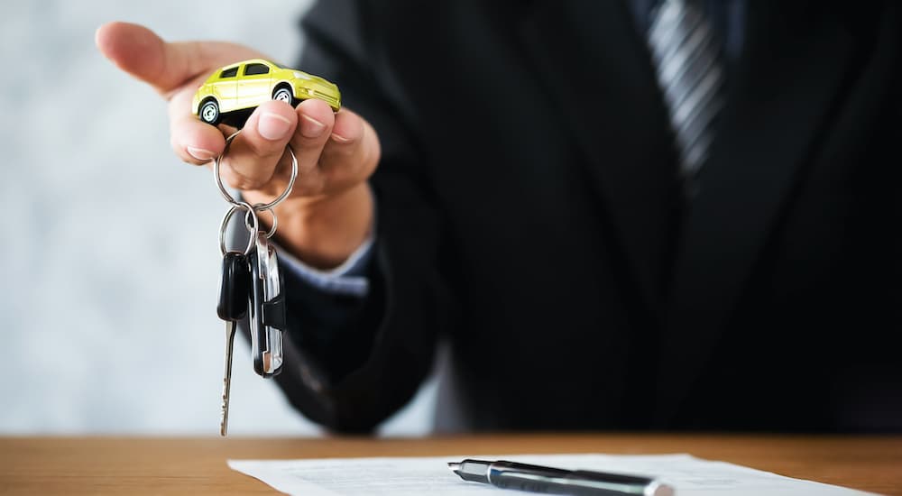 A salesman is shown holding a toy car and set of keys after signing a Nissan lease deal.