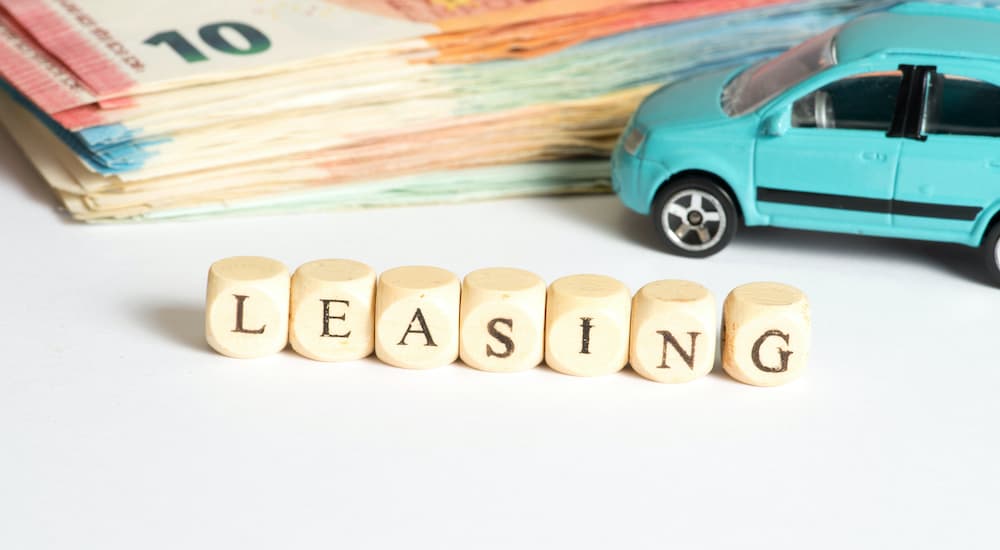 A close up shows blocks that spell leasing with money and a toy car in the background.