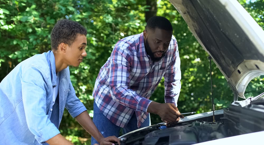 A father and son are going over car basics in the engine bay.