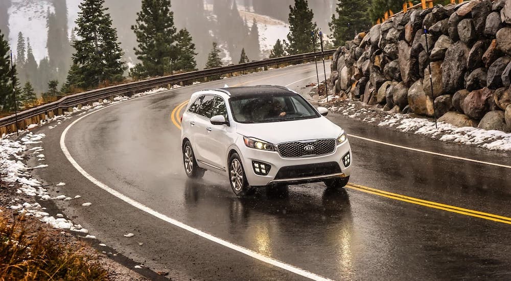 A white 2017 Kia Sorento is driving around a winding road in the snow.