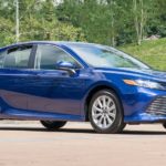 A blue 2017 Toyota Camry is parked in front of grass and trees after leaving a used car dealer.