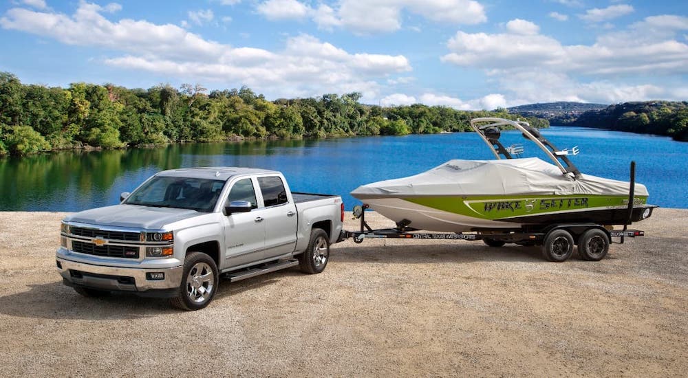 A silver 2016 Chevy Silverado is towing a boat in front of a lake.