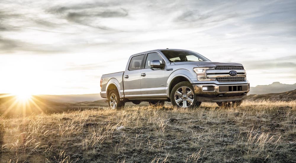 A silver 2016 Ford F-150 is parked in a field in front of a setting sun.
