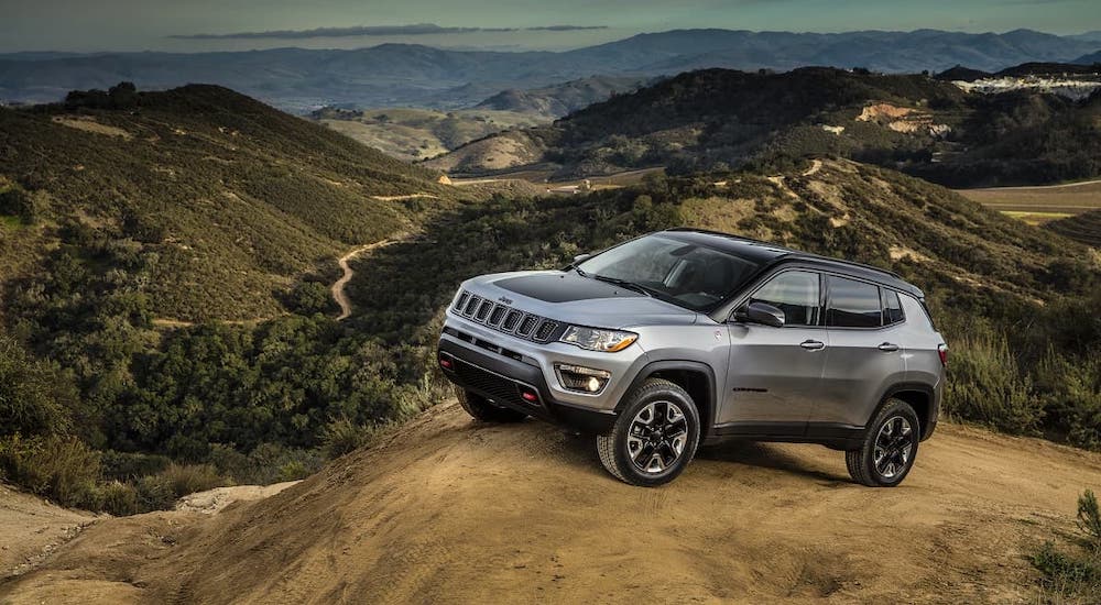 A silver 2020 Used Jeep Compass is parked on a hill overlooking a valley.