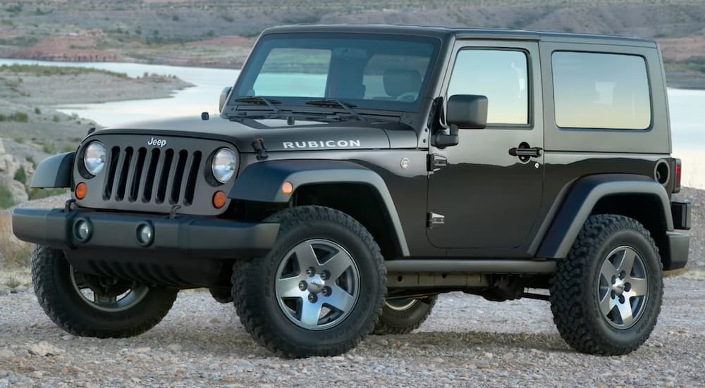 A black used Jeep Wrangler is parked in front of a lake.