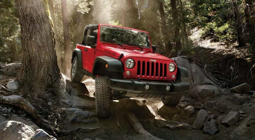 A red 2016 used Jeep Wrangler Rubicon is off-roading in the woods.
