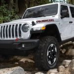 A white 2020 used Jeep Wrangler Rubicon Unlimited is off-roading on a rocky trail in the woods.