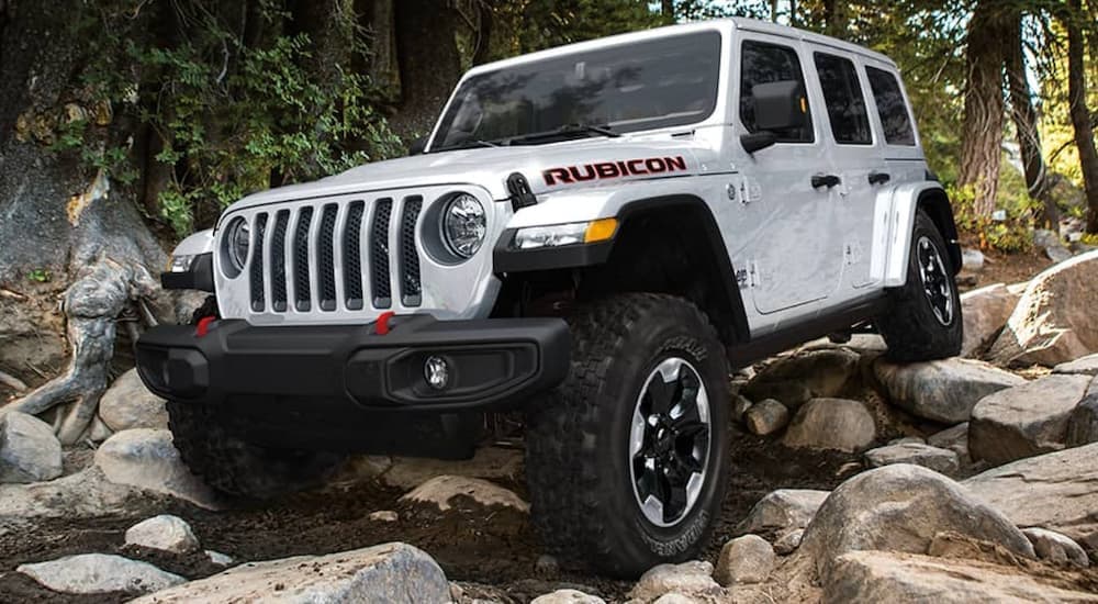 A white 2020 used Jeep Wrangler Rubicon Unlimited is off-roading on a rocky trail in the woods.