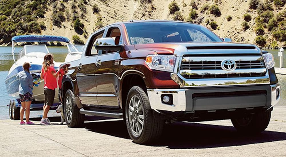 A burgundy 2016 Toyota Tundra is backing a boat into water next to women. 