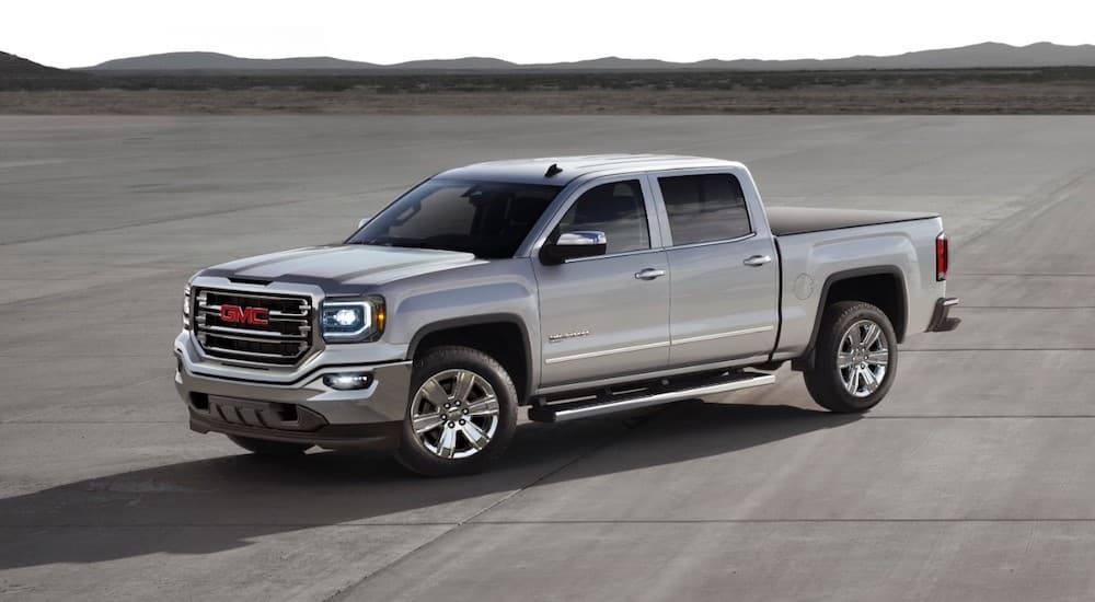 A popular used truck, a silver 2017 GMC Sierra 1500, is parked in an empty lot in front of mountains.