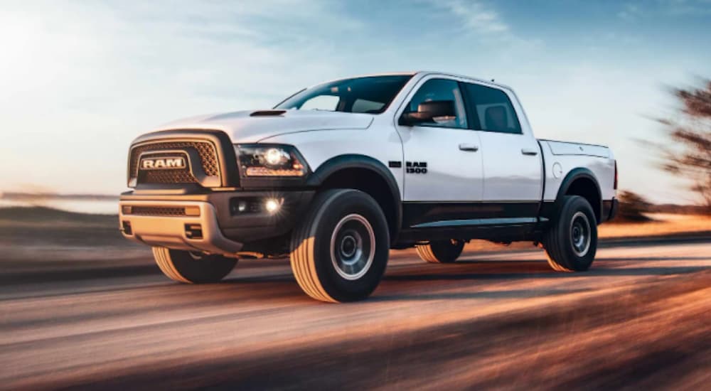 A white 2018 Ram 1500 is driving on a rural road at sunset.