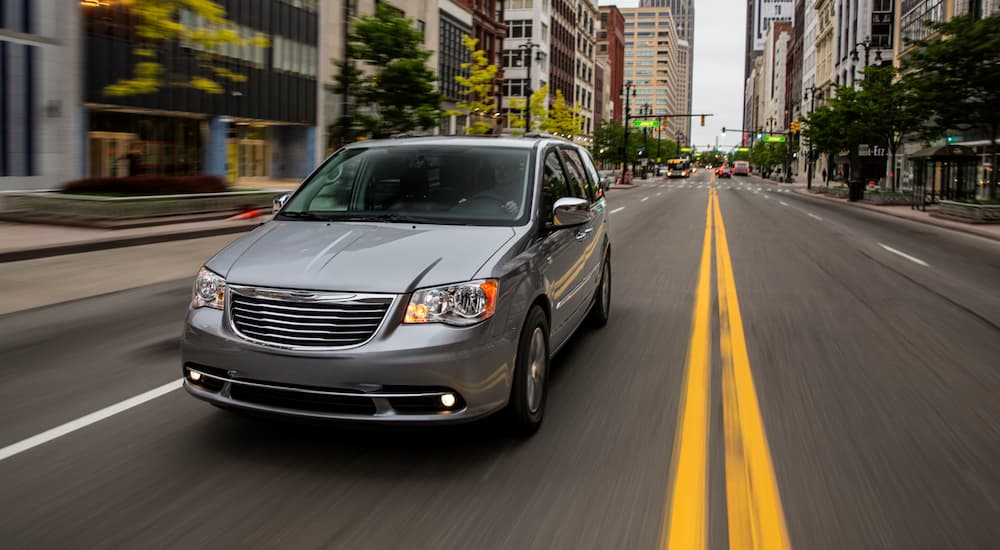 A grey 2016 used Chrysler Town and Country is driving on a city street.