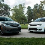 A black and a white 2020 used Chrysler Pacifica are parked in front of a park.