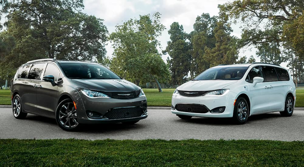 A black and a white 2020 used Chrysler Pacifica are parked in front of a park.