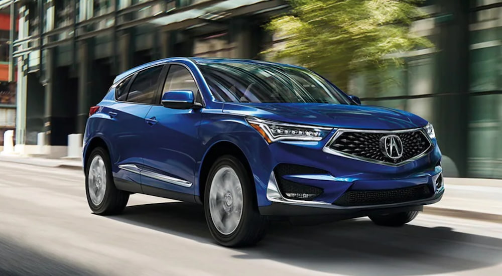 A blue 2021 Acura RDX is driving through a city.