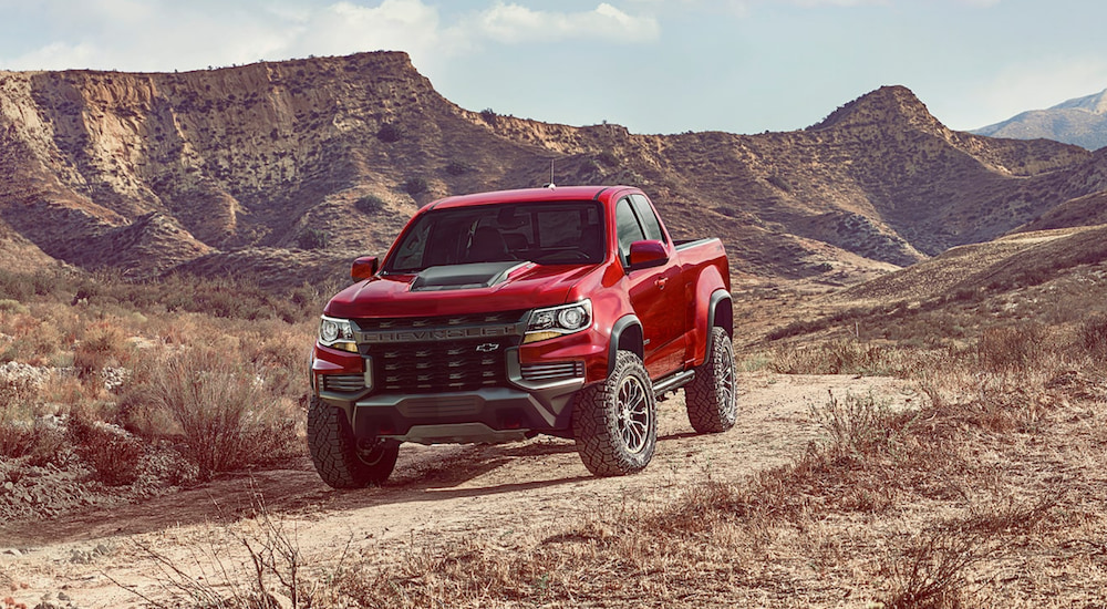 A red 2021 Chevy Colorado ZR2 is driving on a dirt road in the desert. 