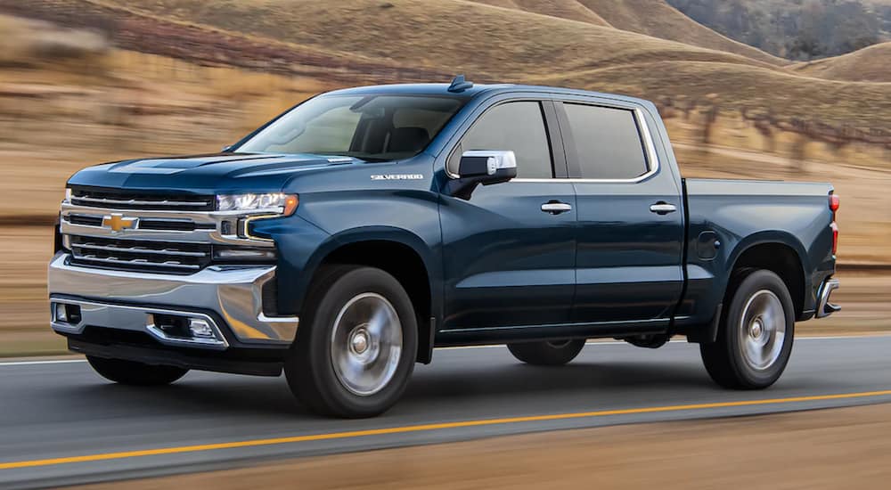 A blue 2021 Chevy Silverado 1500 is shown from the side driving down an open road.