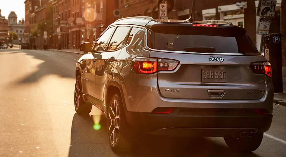 A silver 2021 Jeep Compass is shown from the back driving through a city.