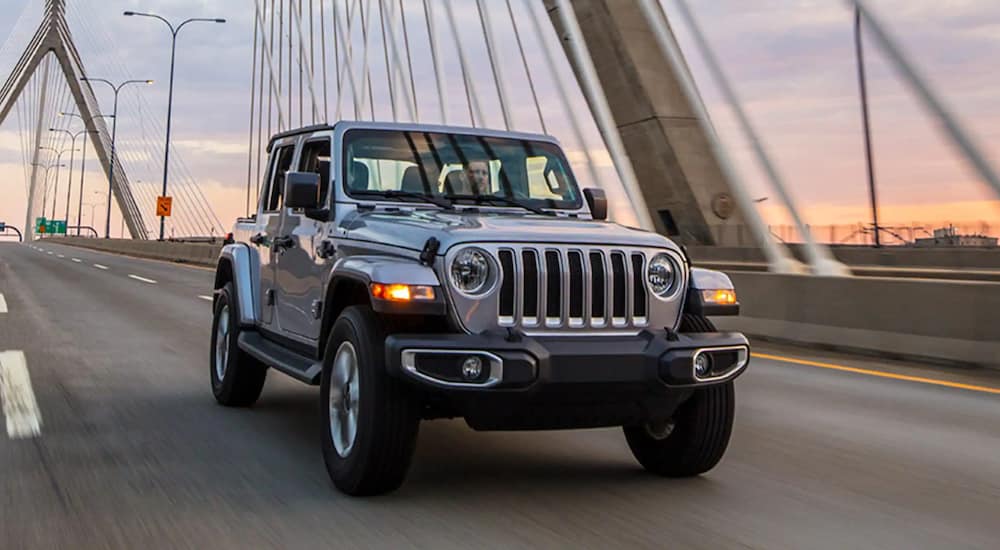 A silver 2021 Jeep Wrangler Unlimited is driving over a bridge at night.