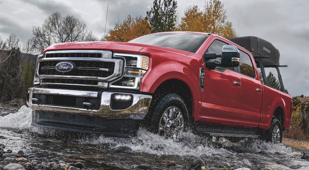 A red 2021 Ford F-250 is crossing a river.